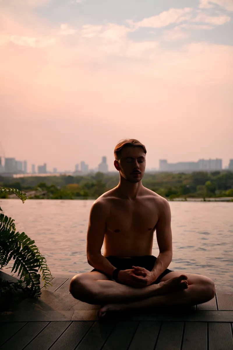 Thomas sitting cross-legged in meditation beside a pool at sunset